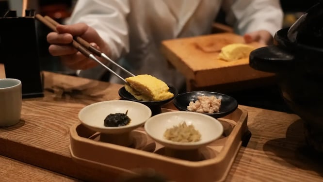 お客様に、ご飯のお供であるだし巻き卵を配膳する様子の写真