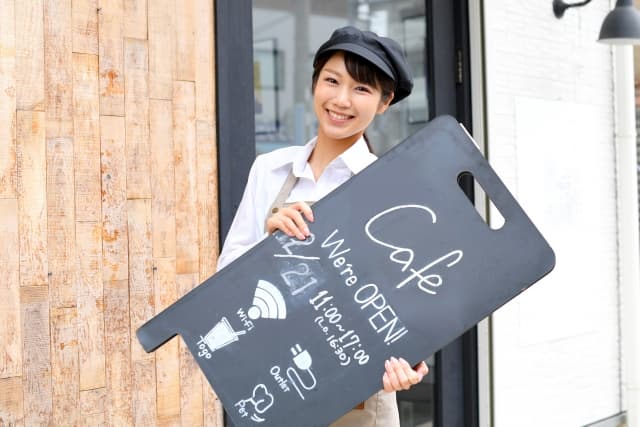 オープンと書かれた看板を持った店員さん