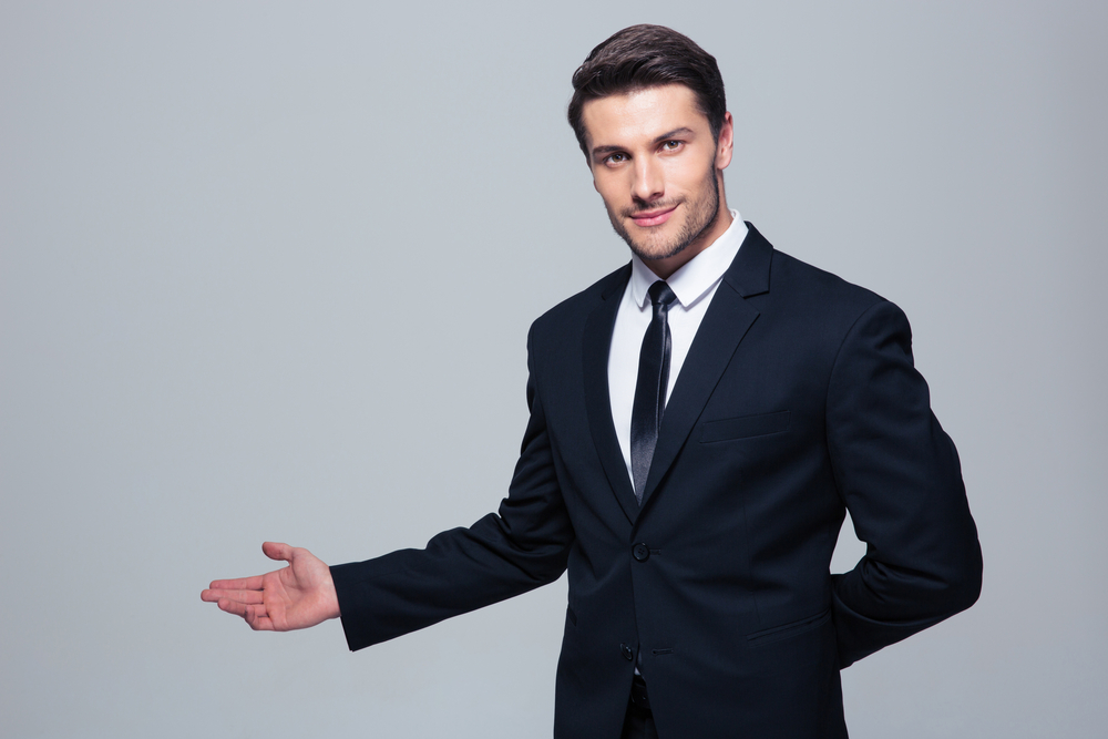 Businessman with arm out in a welcoming gesture over gray background