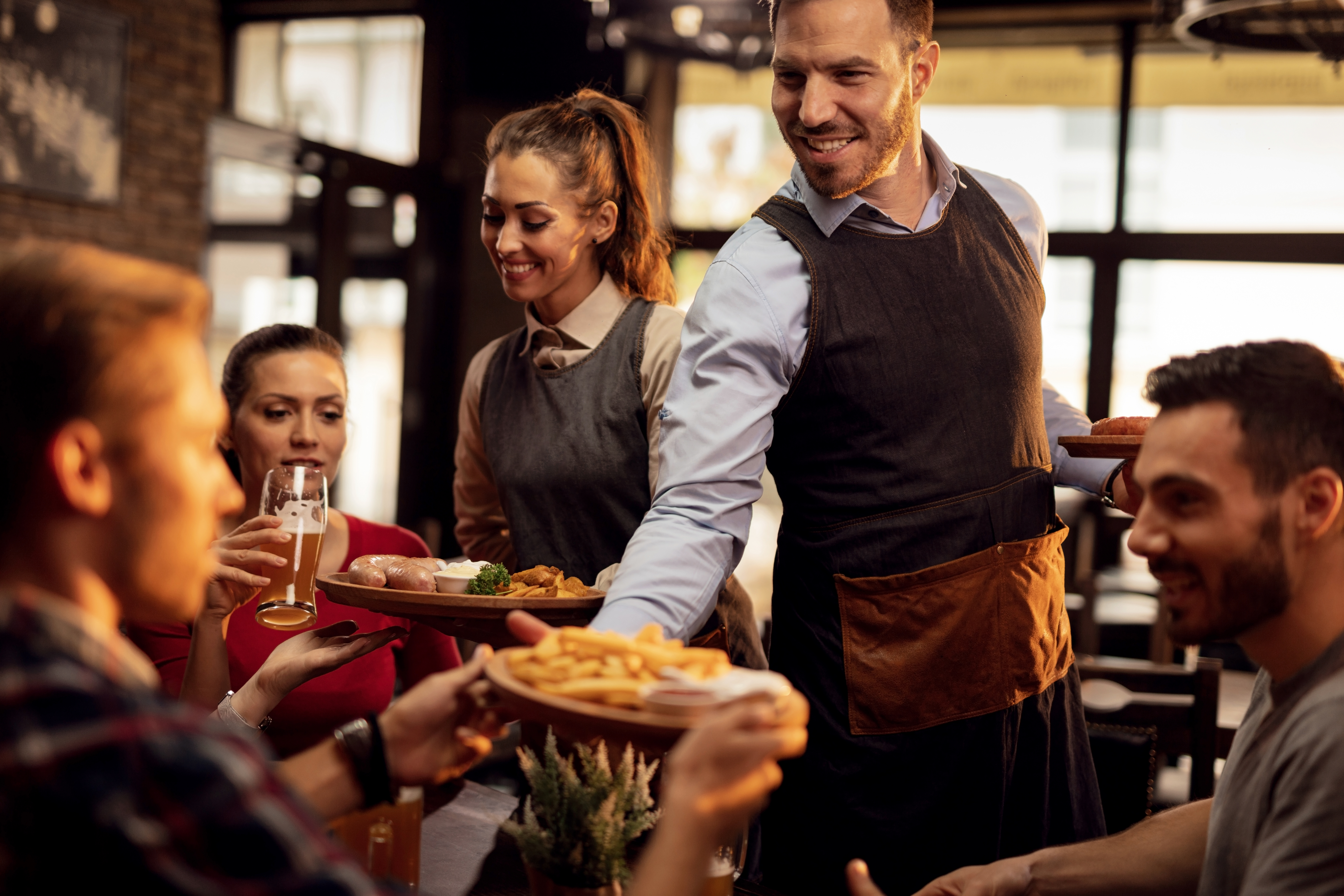 happy-waiters-bringing-food-table-serving-group-friends-restaurant